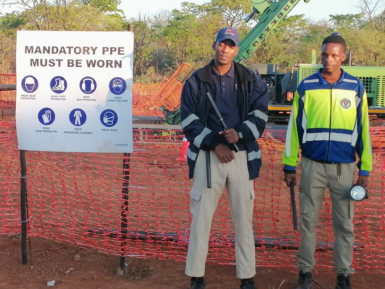 Two Kedith officers beside the mandatory PPE board at the drilling rig
